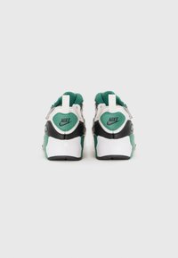 Baskets Nike avec une base blanche, des accents noirs et des détails verts. Présente une semelle texturée et un col rembourré avec le logo à l'arrière.
