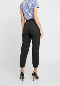 Czarne, zwężane dresy wykonane z miękkiego materiału z elastycznymi mankietami; w połączeniu z niebieską koszulką w tie-dye i czarnymi szpilkami.