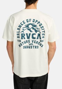 Hvid bomulds t-shirt med en stor blå grafik, der viser bjerge og tekst: "BALANCE AF MODSÆTNINGER RVCA NATURE VERSUS INDUSTRY."