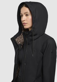 Schwarze Kapuzenjacke mit einem Innenfutter im Leopardenmuster, vorderem Reißverschluss, Druckknöpfen und verstellbaren Kordelzügen. Verfügt über einen strukturierenden Stoff und Logodetails.