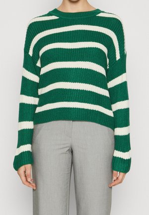 Maglione a righe verdi e bianche con una vestibilità rilassata, maniche larghe e collo rotondo, abbinato a pantaloni grigi chiari.