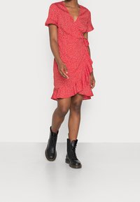 Robe portefeuille rouge à pois blancs, manches courtes à volants, ceinturée à la taille, associée à des bottes de combat noires à lacets.