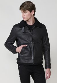 Giubbotto bomber in pelle nera con finitura testurizzata, colletto in finta shearling, due tasche anteriori e chiusura con zip.