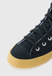 Adidași negri din pânză, cu un tălpic din cauciuc texturat, accente de cusături albe și gauri metalice pentru șireturi.