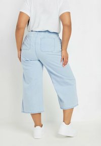 Culottes de mezclilla azul claro con cintura elástica, dos bolsillos traseros y un ajuste relajado, combinados con zapatillas blancas.