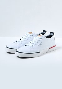 Hvite lerrets-sneakers med gummisåle, med runde snører, logodetalj på siden og en farget aksent på bakhælen.