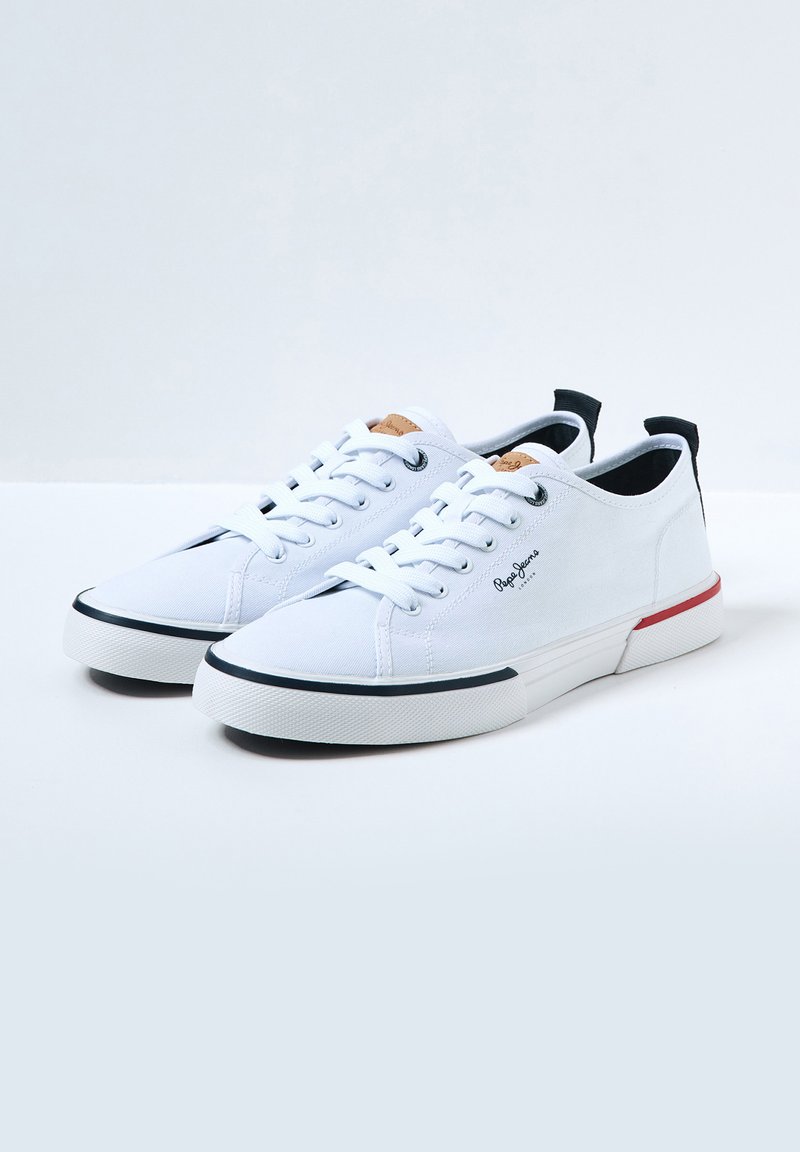 Baskets en toile blanches avec une semelle en caoutchouc, dotées de lacets ronds, d'un logo sur le côté et d'un accent coloré au niveau du talon arrière.