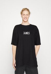 Camiseta negra de corte oversized en algodón, con el texto "KING JAMES" en blanco en el pecho. Mangas cortas y escote redondo.