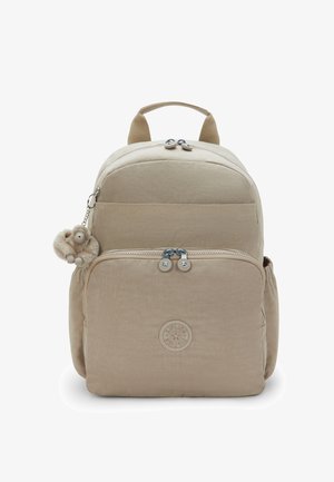 Beige rugzak met een groot voorvak, dubbele ritstrekker, zijvakken, een bovenste handvat en een klein pluchen sleutelhanger in de vorm van een aap eraan bevestigd.