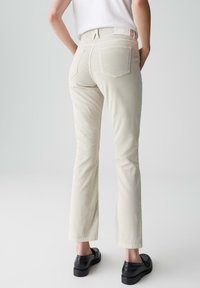 Beige rechte-pijpen broek van een gestructureerde stof, met twee achterzakken en een aansluitende taille, aangevuld met zwarte schoenen.