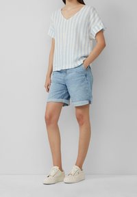 Světle modré a bílé pruhované tričko s krátkým rukávem a výstřihem do V, spárované s džínsovými šortkami a krémovými teniskami. Neformální, uvolněný střih se zahnutaými lemy šortek.