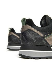 Baskets noires et vertes avec une finition en cuir texturé, un col rembourré et une semelle extérieure gris clair avec des motifs accentués.