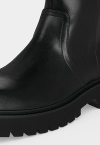 Bottine en cuir noir avec semelle à crampons épaisse et coutures visibles le long de la tige latérale.