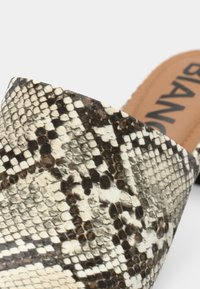 Κοντινό πλάνο λουριού παπουτσιού με σχέδιο δέρματος φιδιού, με υφή που μοιάζει με λέπια, και μέρος από μία ταμπά εσωτερική σόλα με μαύρο κείμενο.