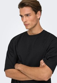 T-shirt noir à manches courtes, col rond, texture douce, coupe décontractée, avec des détails de couture visibles sur les épaules.