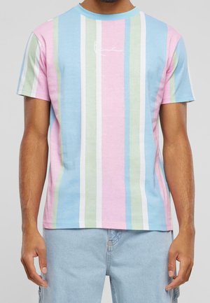 Mężczyzna w pastelowej koszulce z krótkim rękawem w pionowe paski w kolorach niebieskim, różowym, zielonym i białym oraz w jasnoniebieskich dżinsach.