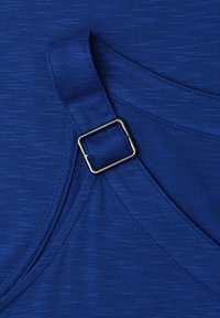 Tissu bleu avec une sangle ajustable cousue présentant une boucle rectangulaire argentée sur un vêtement.
