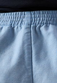 Hele sinine elastne vöökoht pehmetel kangast pükstel, millel on nähtav õmblus keskel, kantud tumedat värvi rõiva peale.