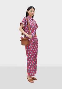 Multicolored shirt dress with geometric print in pink, red, and blue. Paired with a brown crossbody bag and brown flat sandals.