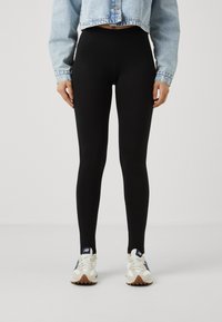 Melnas augstās leggingas, izgatavotas no elastīga materiāla, kopā ar gaismas zilā krāsā apgriezto džinsas jaku un baltām sneakerām ar akcentiem.