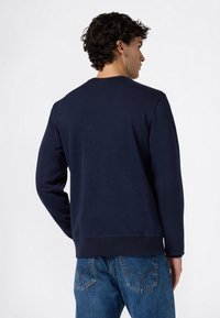 Sudadera azul marino con cuello redondo y puños acanalados. Textura lisa, ajuste estándar, combinada con jeans de mezclilla azul claro.