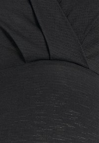 Svart plagg med en texturerad yta, funktioner lager-på-lager drapering och en åtsittande design. Materialet har en subtil lyster och ett ribbat mönster.