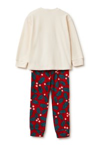Top de forro polar crema de manga larga combinado con pantalones de pijama rojos con un patrón de acebo verde y bayas blancas, textura suave, ajuste informal.