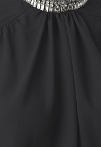 Top in tessuto nero con un design plissettato, caratterizzato da un'applicazione metallica sul colletto composta da pezzi lucidi intrecciati.