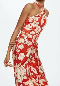 Rode haltertop met bloemenprint en knoopdetail, gecombineerd met bijpassende wijde broek met een beige bloemenpatroon en een gestrikte taille.