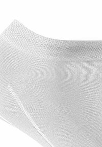 Biała skarpetka z elastycznego materiału z teksturowanym mankietem. Materiał wydaje się gładki i lekki, zapewniając ciasne dopasowanie wokół kostki.