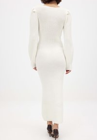 Pikk, valge soonikkoes kleit pikade varrukatega ja kehakujulise silueti, millel on õlavarre detailid ja sile tekstuur. Kandmiseks tumedad kõrged kontsad.