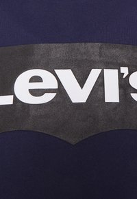 T-shirt bleu marine avec un grand motif noir comprenant le mot "Levi's" en lettres blanches en gras sur la poitrine. Texture lisse.