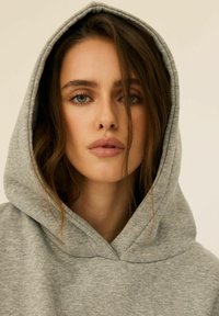 Szara bluza z kapturem o miękkiej fakturze. Posiada przestronny kaptur i prosty, nieozdobiony design. Gładki materiał o luźnym kroju.