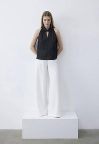 Black halter top with vertical stripes, featuring a keyhole detail. Paired with wide-leg white trousers, both are set against a light background.