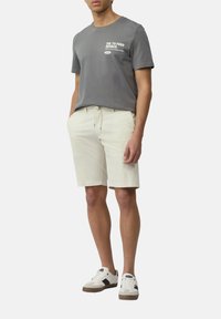 Graues Baumwoll-T-Shirt mit weißem Grafikdruck, kombiniert mit hellbeigen Shorts und weißen Sneakers mit schwarzen Akzenten. Lässiger Schnitt.