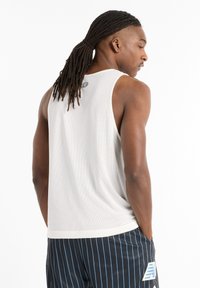 Mesh athletic tank top in white, featuring a crew neck, back logo detail, and a loose fit. Worn with black pinstriped shorts.