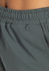 Tejido gris y elástico con una cinturilla elástica; presenta sutiles pliegues y una textura suave, diseñado para la comodidad y la facilidad de movimiento.