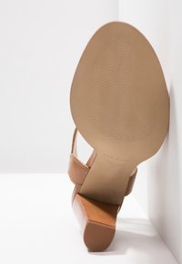 Ruske sandale na petu s dizajnom križnog remena. Gornji dio od glatke kože, reljefna blok peta i fleksibilna, rebrasta podloga.