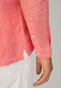 Camicia di lino rosa a maniche lunghe con polsini abbottonati, fessure laterali e vestibilità comoda. Il tessuto ha un aspetto leggermente strutturato.