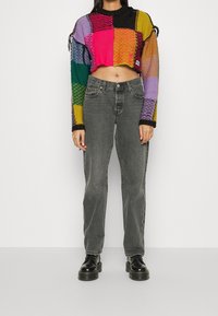 Haken trui met een multicolore patchwork ontwerp, cropped lengte en zwarte accenten, gecombineerd met grijze rechtzittende jeans en zwarte laarzen.