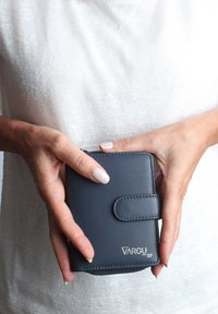 Navy blue leather wallet with stitched accents, a snap closure, and a logo in silver. Held in hands against a light-textured background.