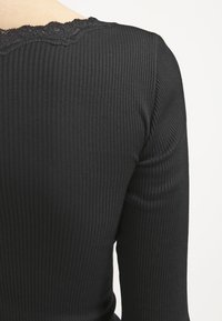 Czarny prążkowany top z długim rękawem i koronkowym akcentem przy dekolcie. Materiał jest gładki, a krój dopasowany.