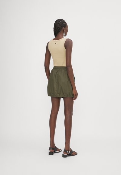 Beige ribbed tank top paired with an olive green, elastic-waist mini skirt. Black, strappy sandals complete the outfit.