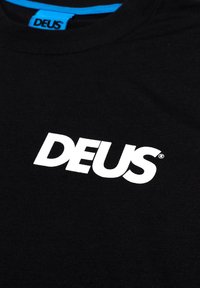 Black cotton T-shirt with a round neckline, featuring a prominent white "DEUS" logo in bold font. Smooth texture, minimalistic design.