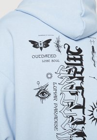 Jasnoniebieska bluza z kapturem z czarnymi grafikami, w tym ćma, oko i tekst. Materiał wydaje się miękki i ma luźny krój.