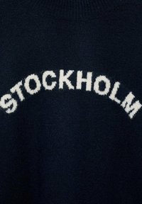 Mornarska jopica z belim napisom "STOCKHOLM" v ukrivljenem, krepko pisanem fontu. Mehka tekstura z rebrastim detajlom ovratnika.