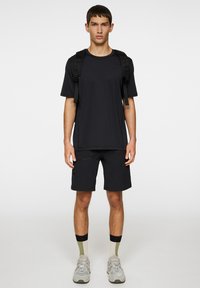 Svart kortärmad t-shirt och svarta shorts, båda med en slät textur. Inkluderar en ficka med dragkedja och bärs med grå sneakers och mönstrade strumpor.
