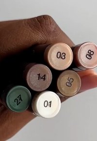 Sett med seks kosmetiske penner holdt i en hånd. Fargene inkluderer hvit, lys beige, brun og grønn. Hver penn er nummerert på enden.