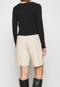 Svart randig långärmad topp med en scalloped nederkant, i kombination med beige shorts och knähöga svarta stövlar. Enkel, åtsittande design med en texturerad yta.
