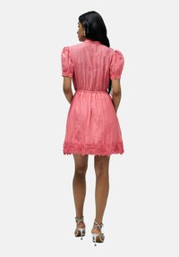 Vestido rosa con mangas cortas abullonadas, tejido texturizado, cintura ceñida y adornos de encaje floral en el dobladillo. Llevado con sandalias plateadas de tiras.